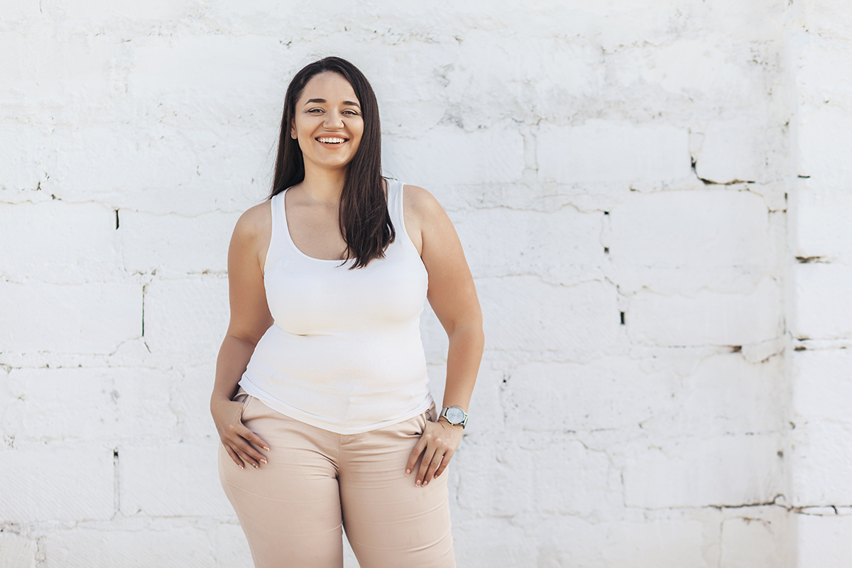 plus size model dressed in white shirt posing over brick wall