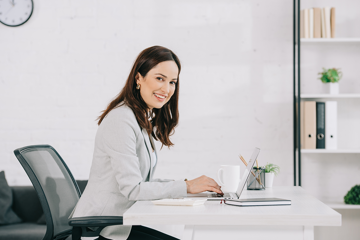 smiling secretary looking at camera while sitting at workplace in office
