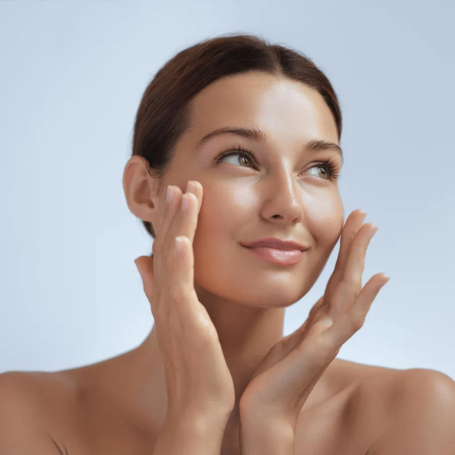 Skincare. Woman with beautiful face touching healthy facial skin. Beautiful portrait of smiling Asian girl model with natural makeup enjoys glowing hydrated skin on blue background closeup.