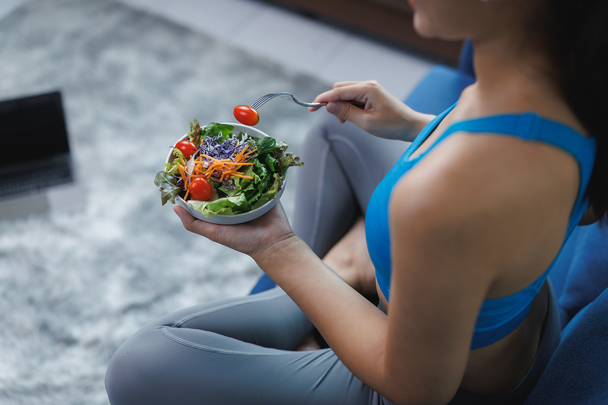 young woman eating healthy salad after workout at home